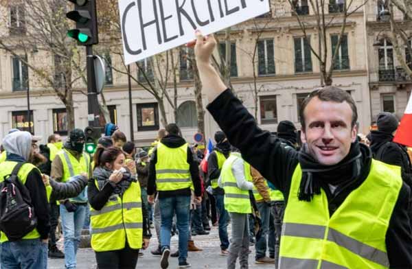 Manifestant en gilet jaune portant un masque à l'éffigie d'E. Macron.