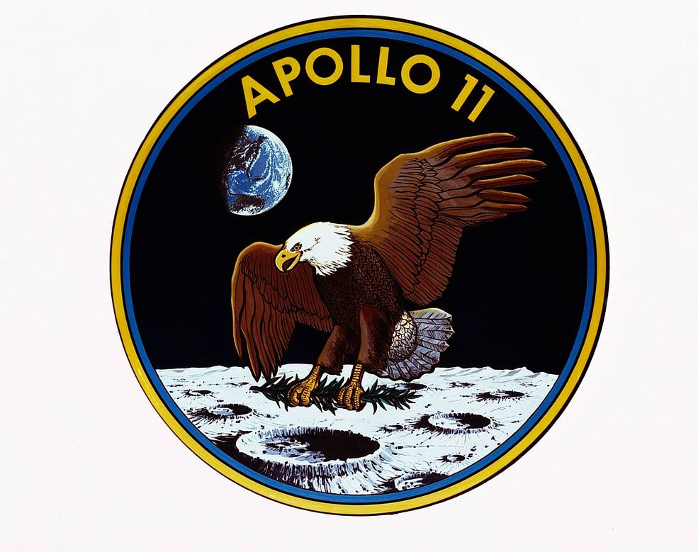 Logo Apollo 11  Sur l'insigne de la mission, un pygargue,   emblème des États-Unis, porte des rameaux d'olivier dans ses serres